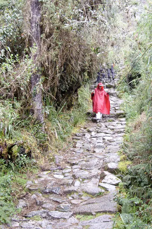 Woman in red poncho carefully descending a wet, stone path