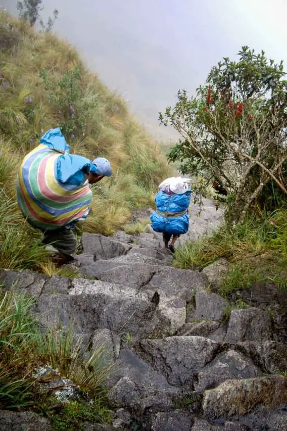 Our porters descend steep stone stairs wearing rubber sandals and carrying enormous packs.