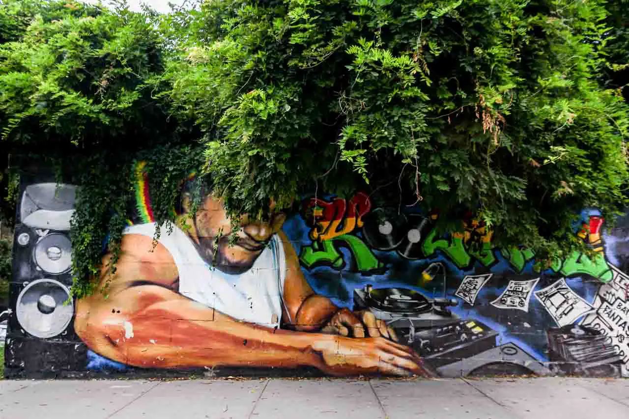 Mural tribute to DJ Kool Herc with bush growing over the wall