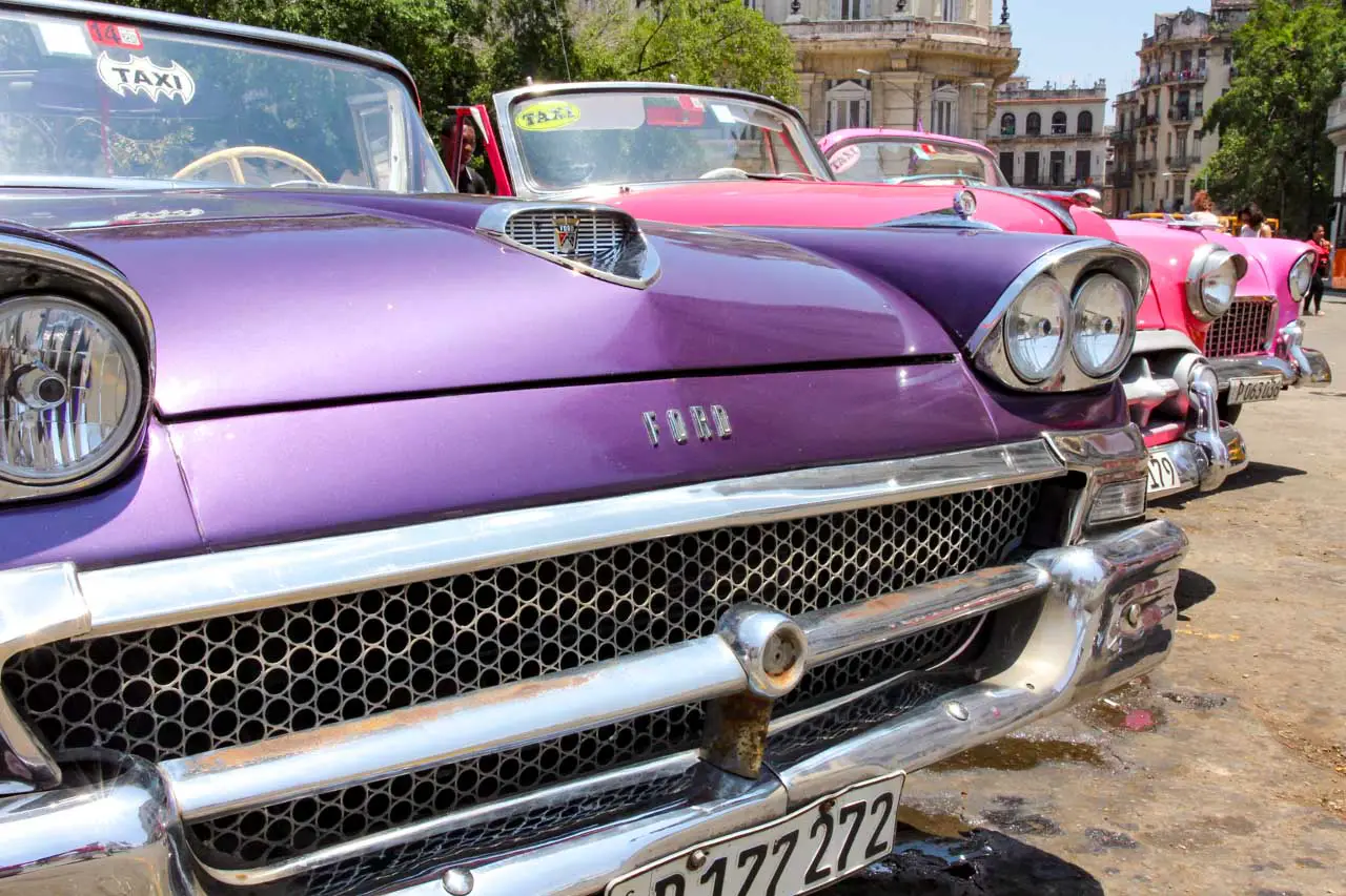 A line up of classic cars beginning with a purple Ford