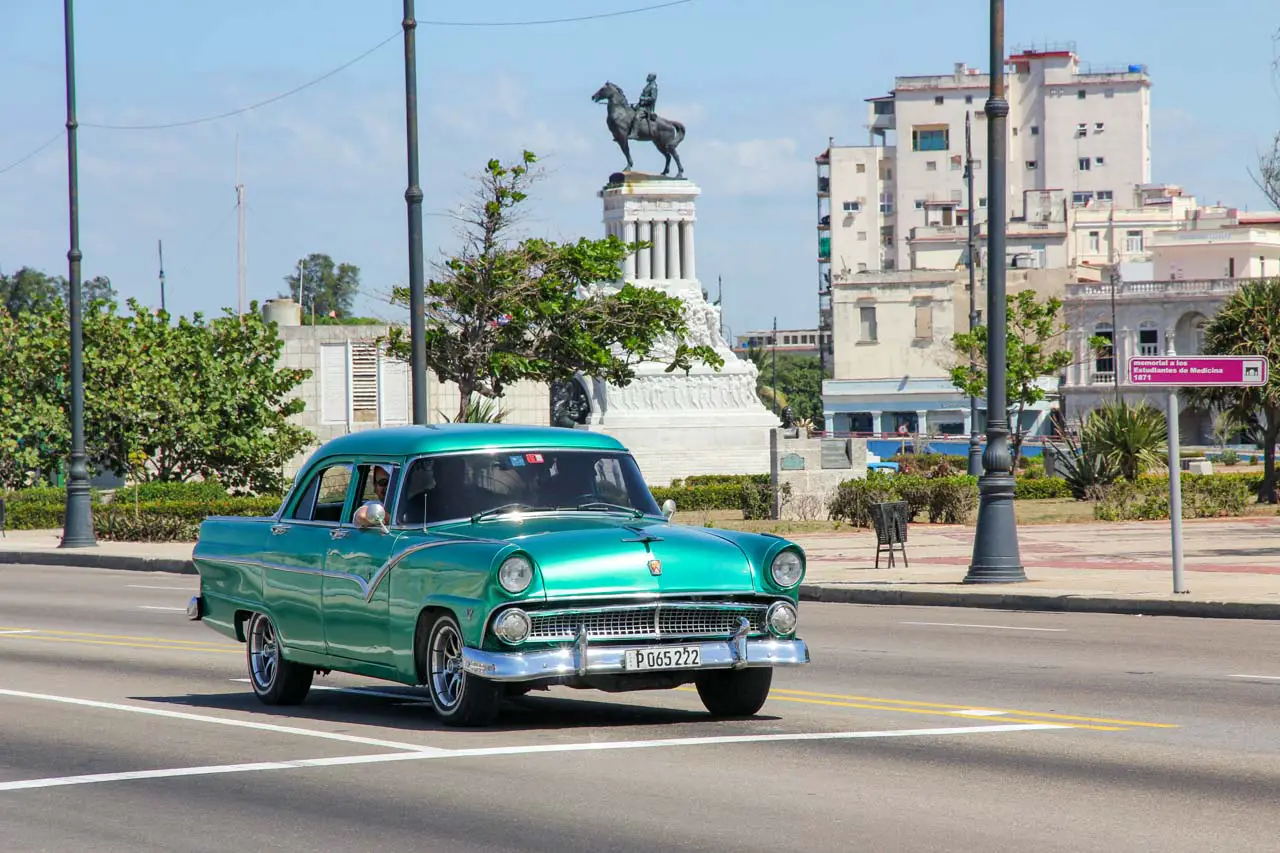 Aqua, vintage Ford Fairlane stopped at an intersection, with monument in background