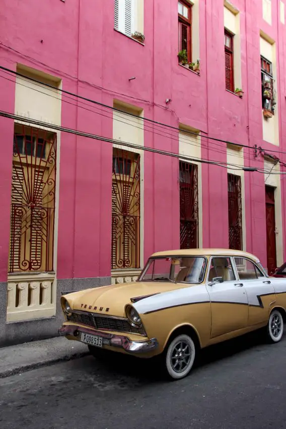 Taurus in beige and white parked infront of a pink building