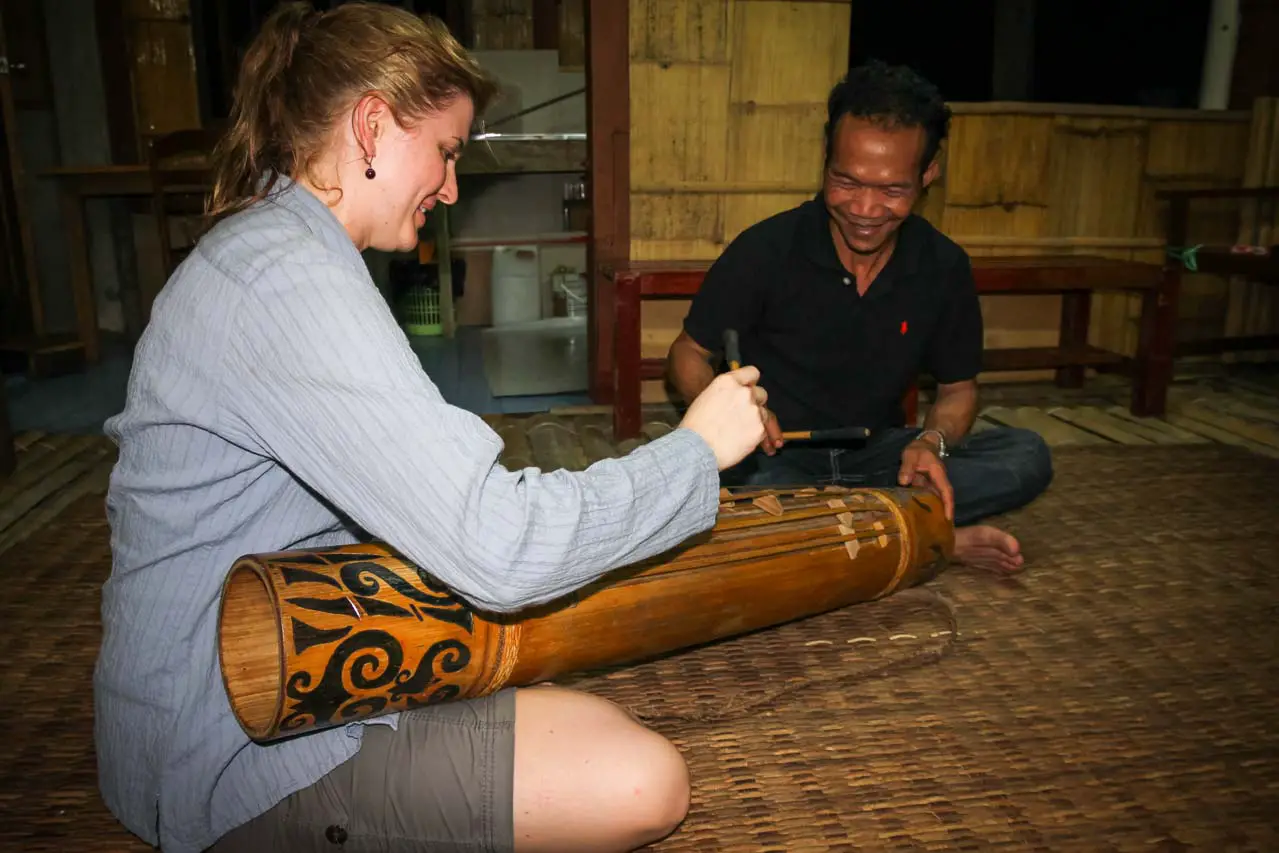 Woman learning to use musical instrument, seated on floor with teacher