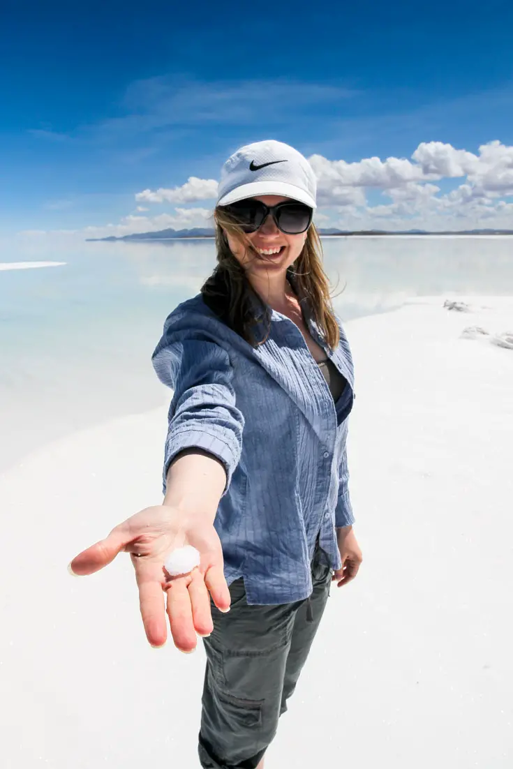 Woman holding out a handful of salt on sunny salt flat with mountains in the distance