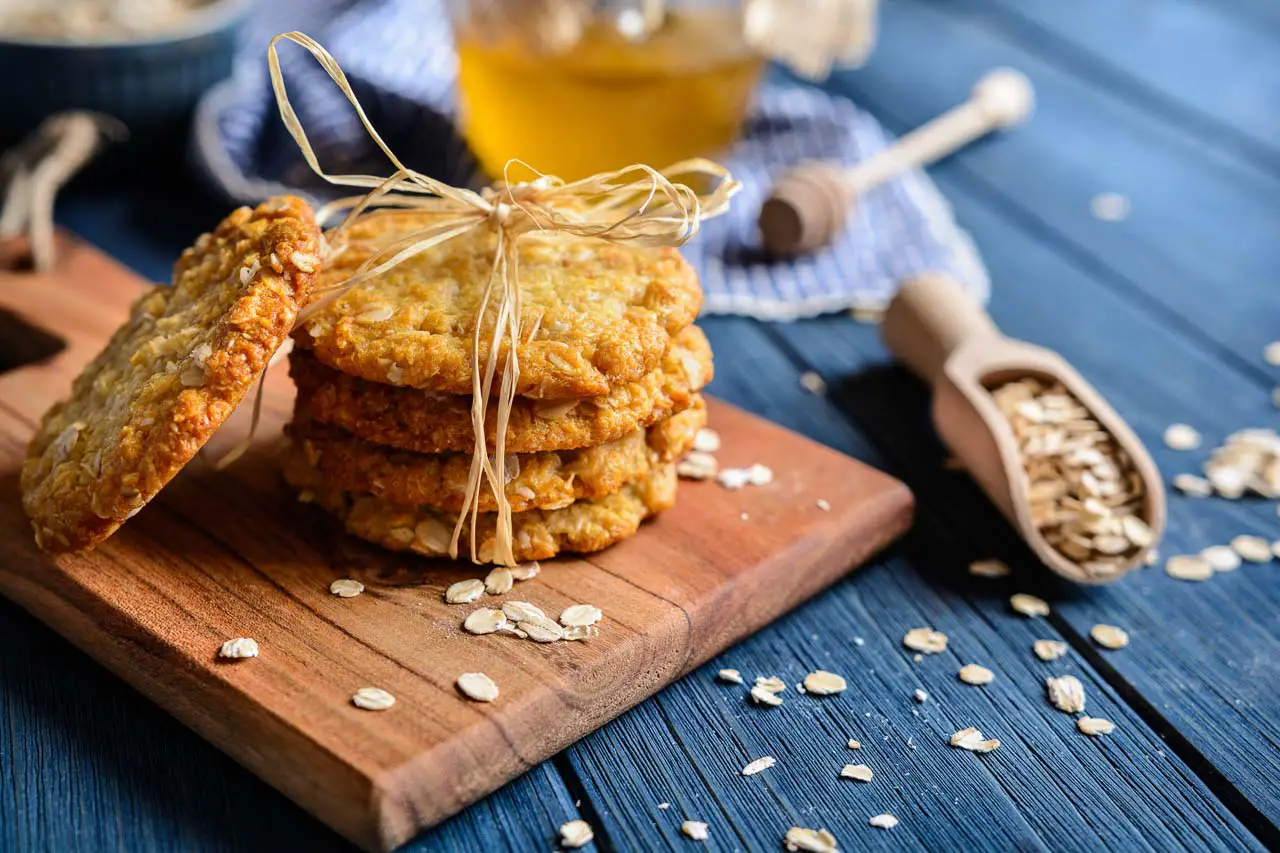 ANZAC biscuits tied with brown string on a wooden board with a spoonful of oats and honey in background