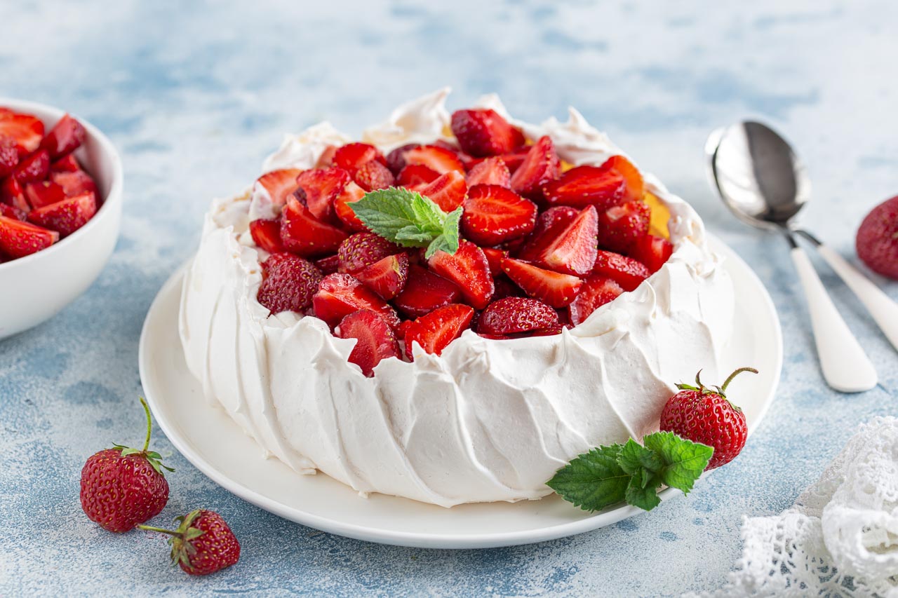 Pavlova with strawberries on white plate and blue tabletop