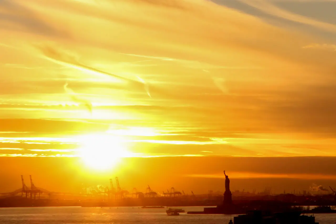 Sunset view of the Statue of Liberty and silhouette of industrial port