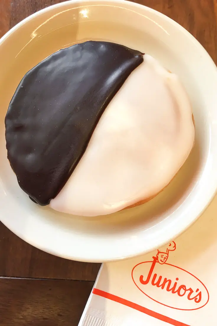 Black and white cookie on white plate with Junior's-branded napkin underneath