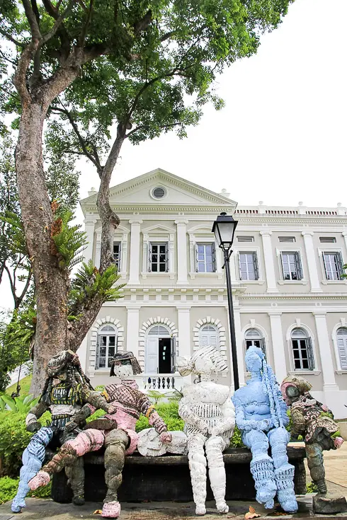 Photo of National Museum of Singapore with sculpture of peple on park bench in foreground
