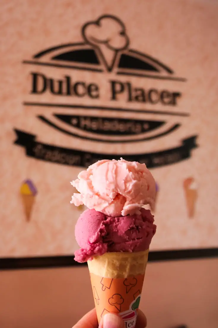 Scoops of two different pink-coloured ice creams in a cone infront of a sign called Dulce Placer
