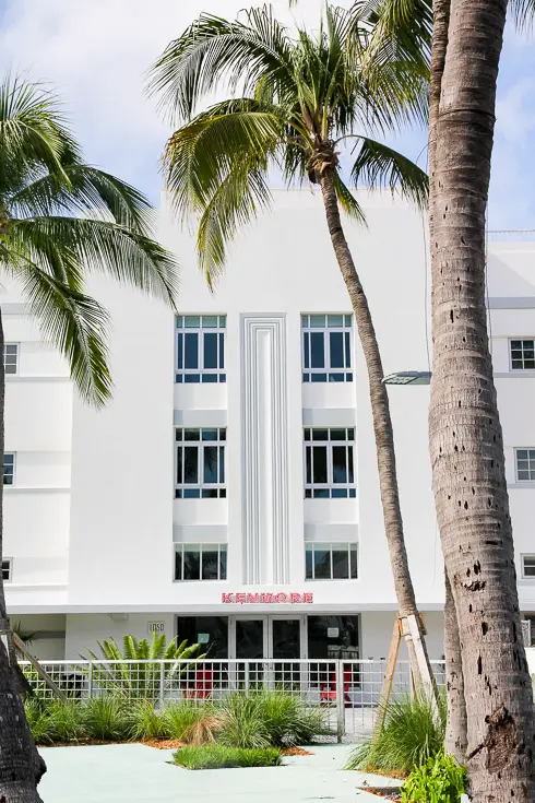 Facade of white art deco building with palm trees in foreground