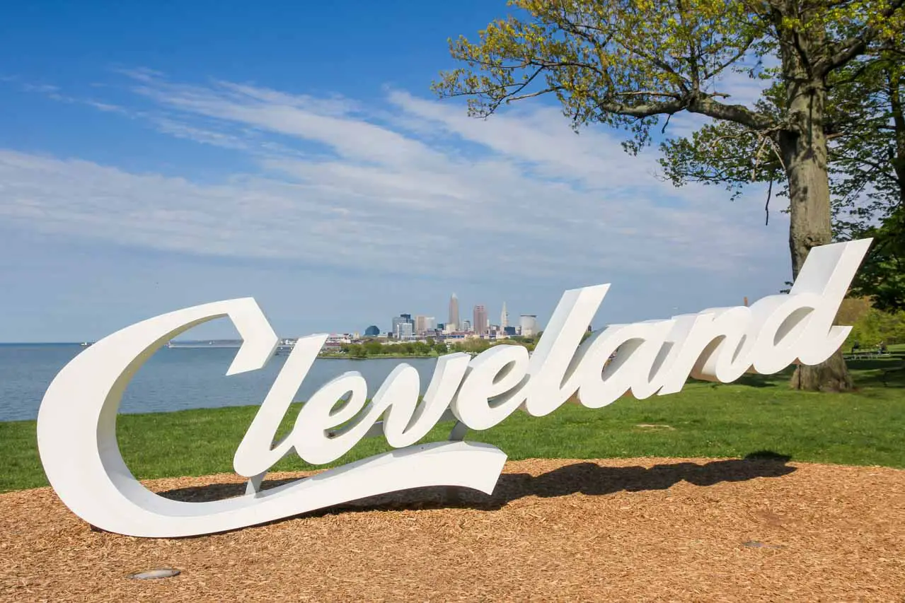 Sign reading "Cleveland" in parkland with Lake Erie and city skyline in the background