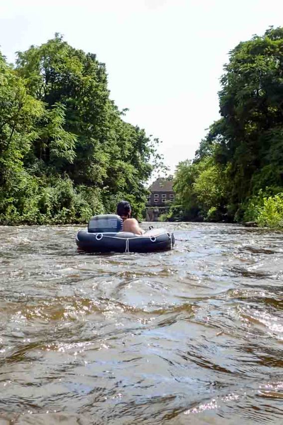 Person in tube floating down river framed by trees