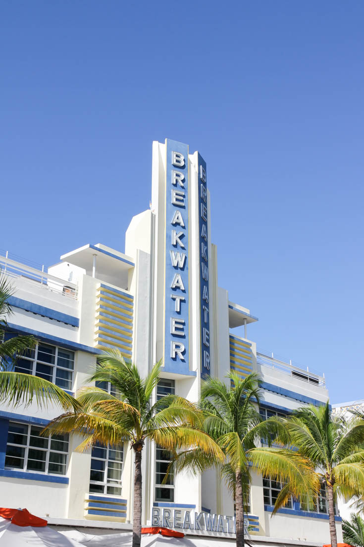 Art Deco spire that tops the facade of Breakwater with palm trees in foreground and blue sky behind