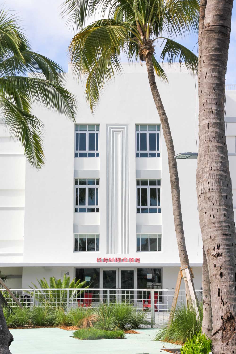 Facade of white art deco building with palm trees in foreground