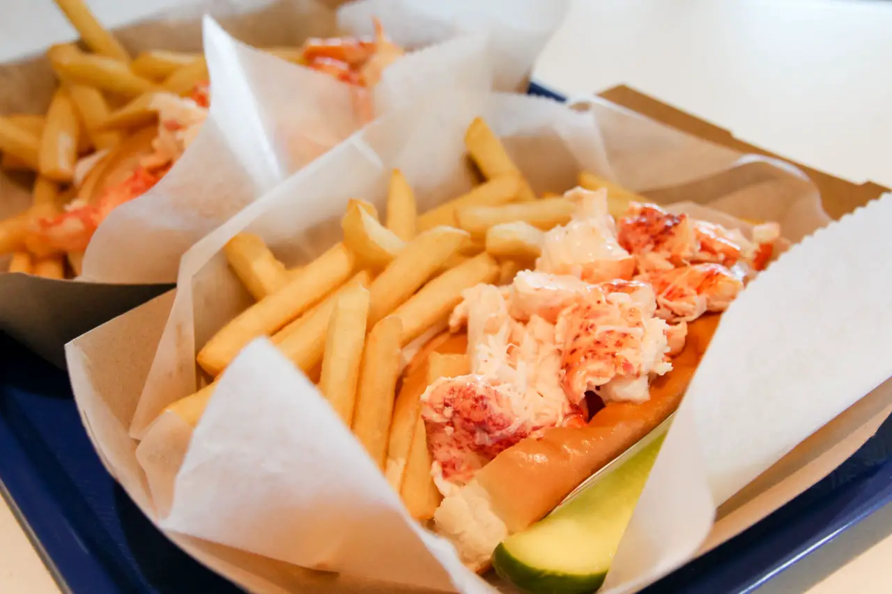 Lobster roll served in white paper with fries and pickle