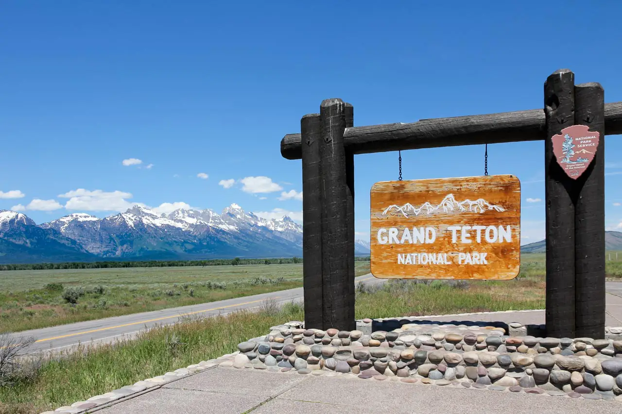 Grand, wooden sign reading "Grand Teton National Park" with mountains in the background