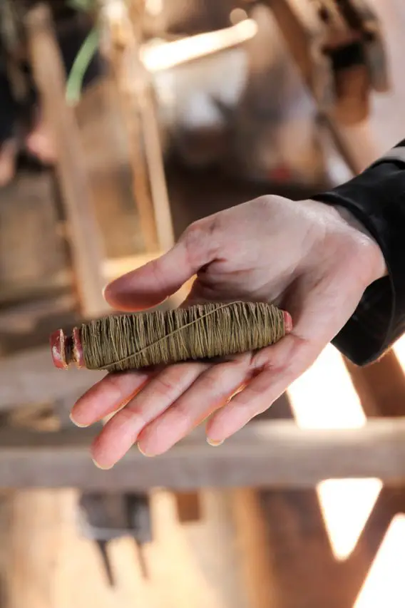 A woman's hand holding a spool of undyed lotus thread