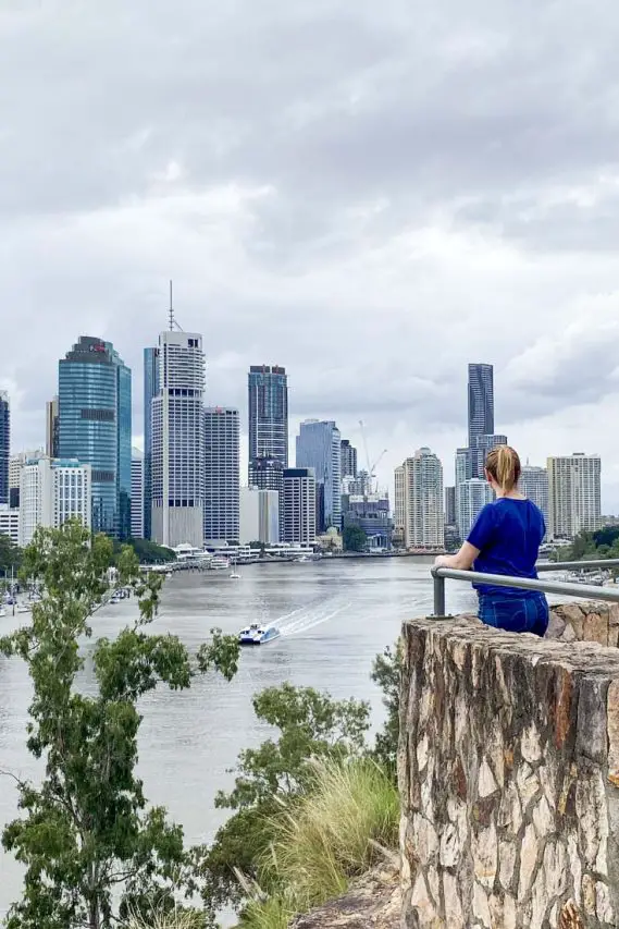 Woman in blue t-shirt overlooking river towards city skyline 