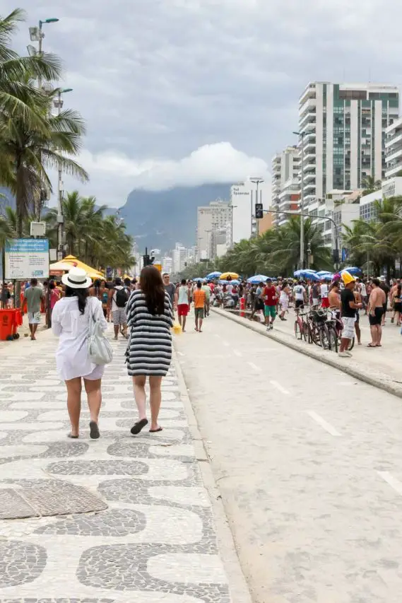 Revelers in the street with mosaic sidewalks, palm trees and mountains in the background