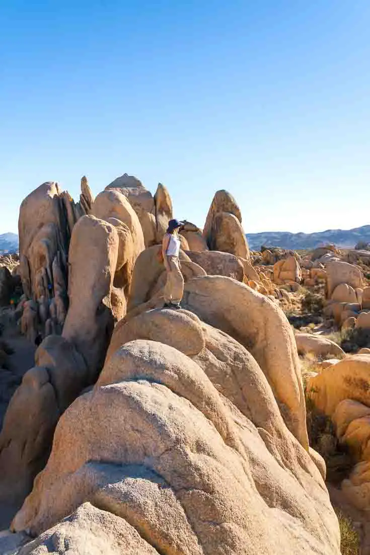 Woman standing on sandstone rock formation looking out at landscape and blue sky