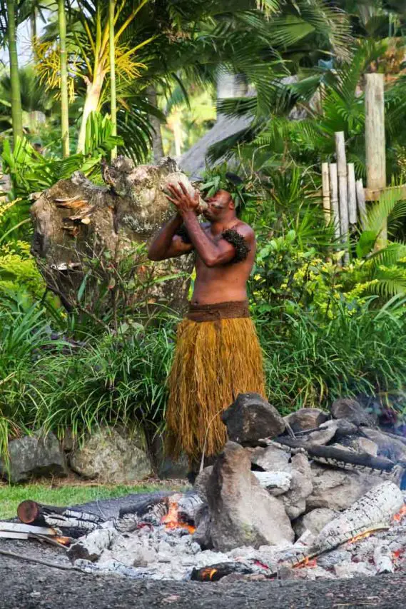 Man in traditional Melanesian dress, blowing on a conch shell