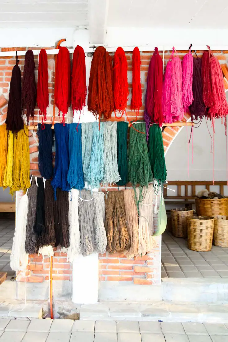 Threads of various colours hanging outside weaving workshop with woven baskets in background