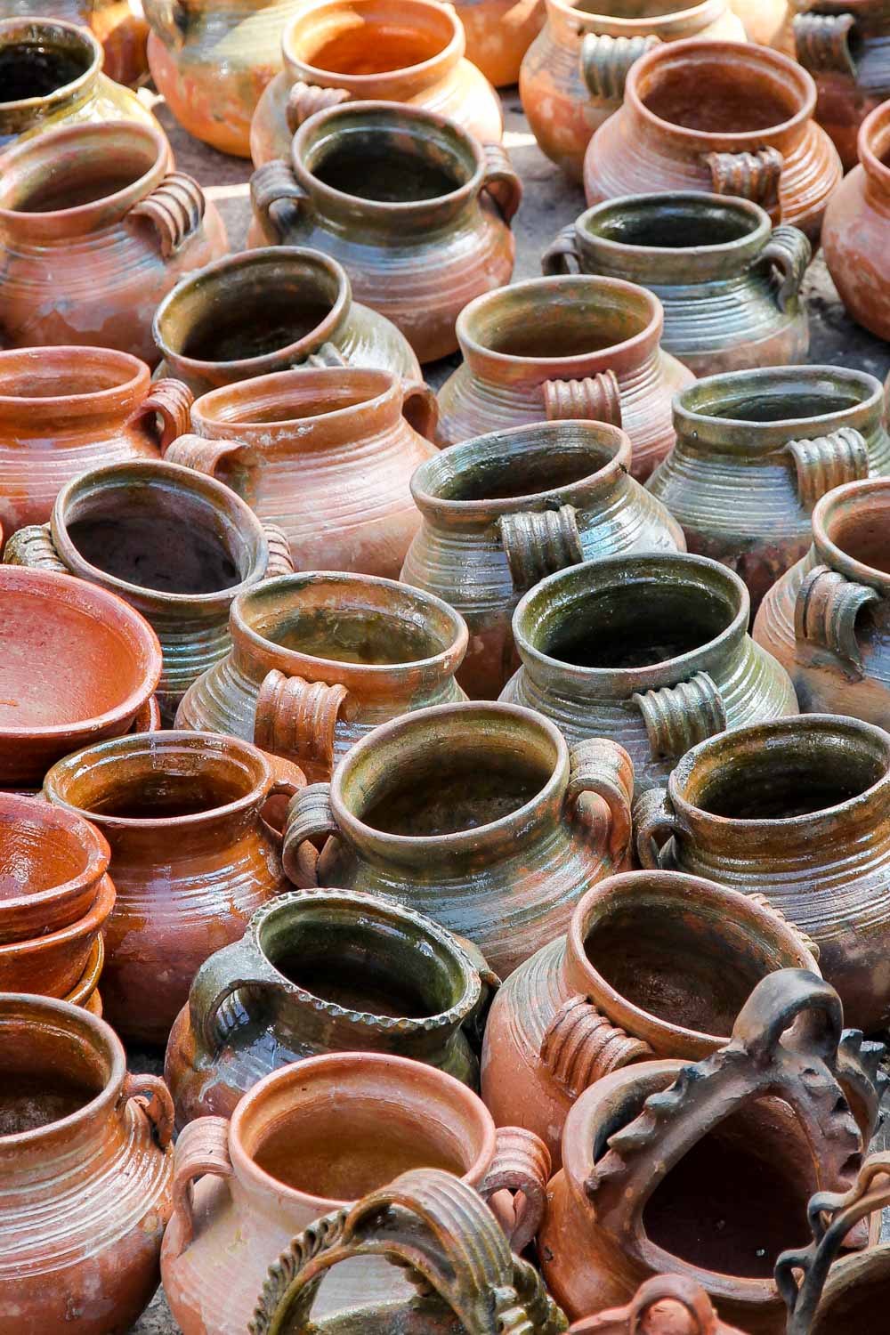 A close up of many similar pottery urns in green and orange glazes