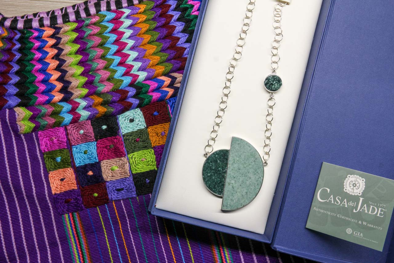 Jade and silver necklace inside blue gift box on an embroidery-decorated huipil