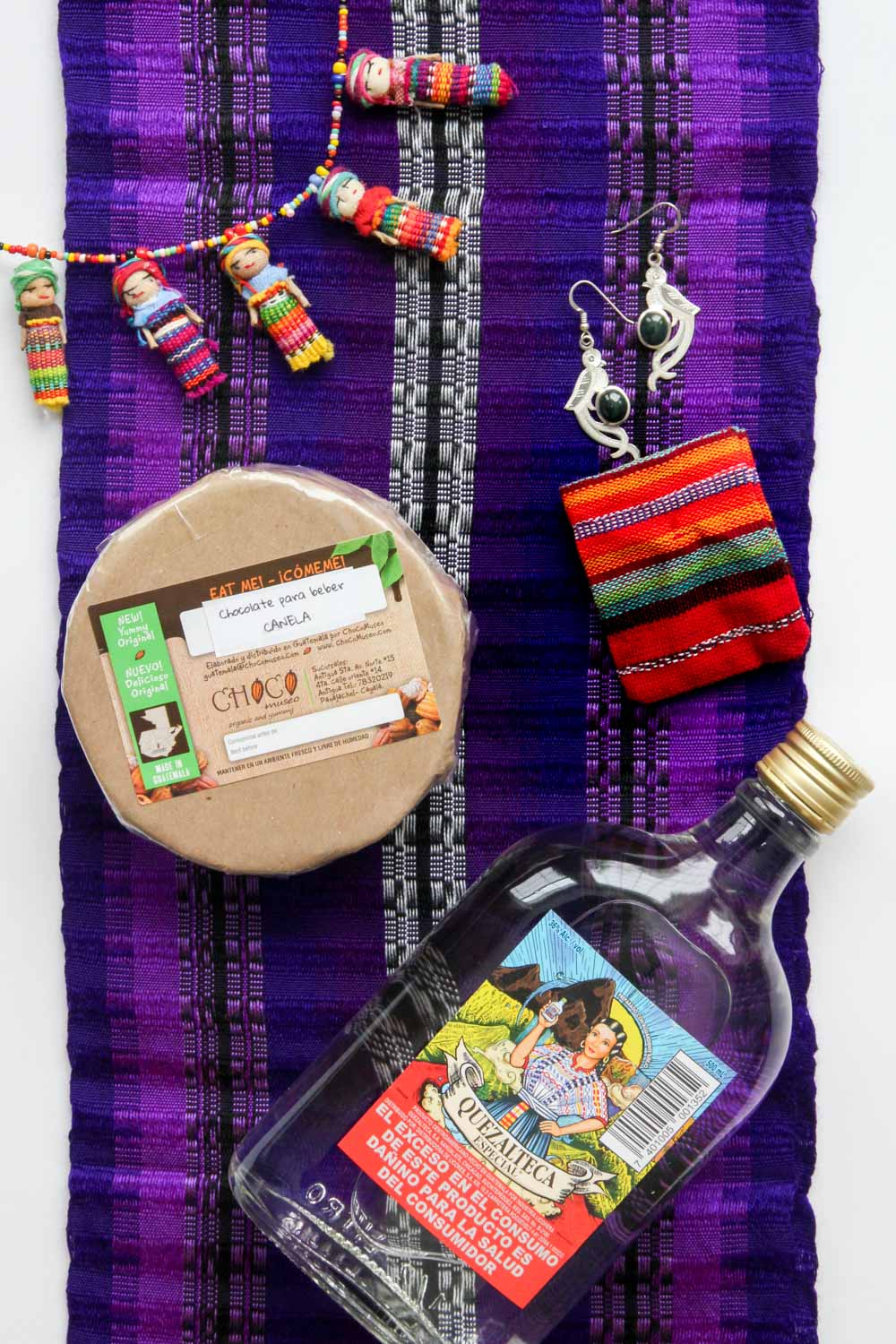 Image of souvenirs from Guatemala, laid out on a purple woven scarf including chocolate, rum and jewellery