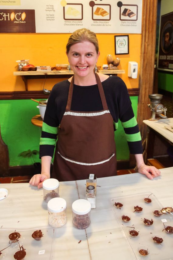 Woman in apron standing at benchtop with filled chocolate moulds