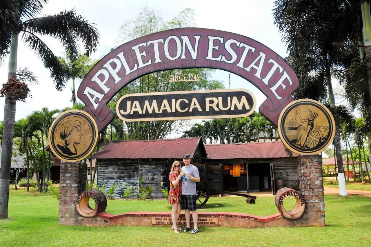 Couple saying cheers over rum cocktails under an outdoor Appleston Estate Jamaica Rum sign 