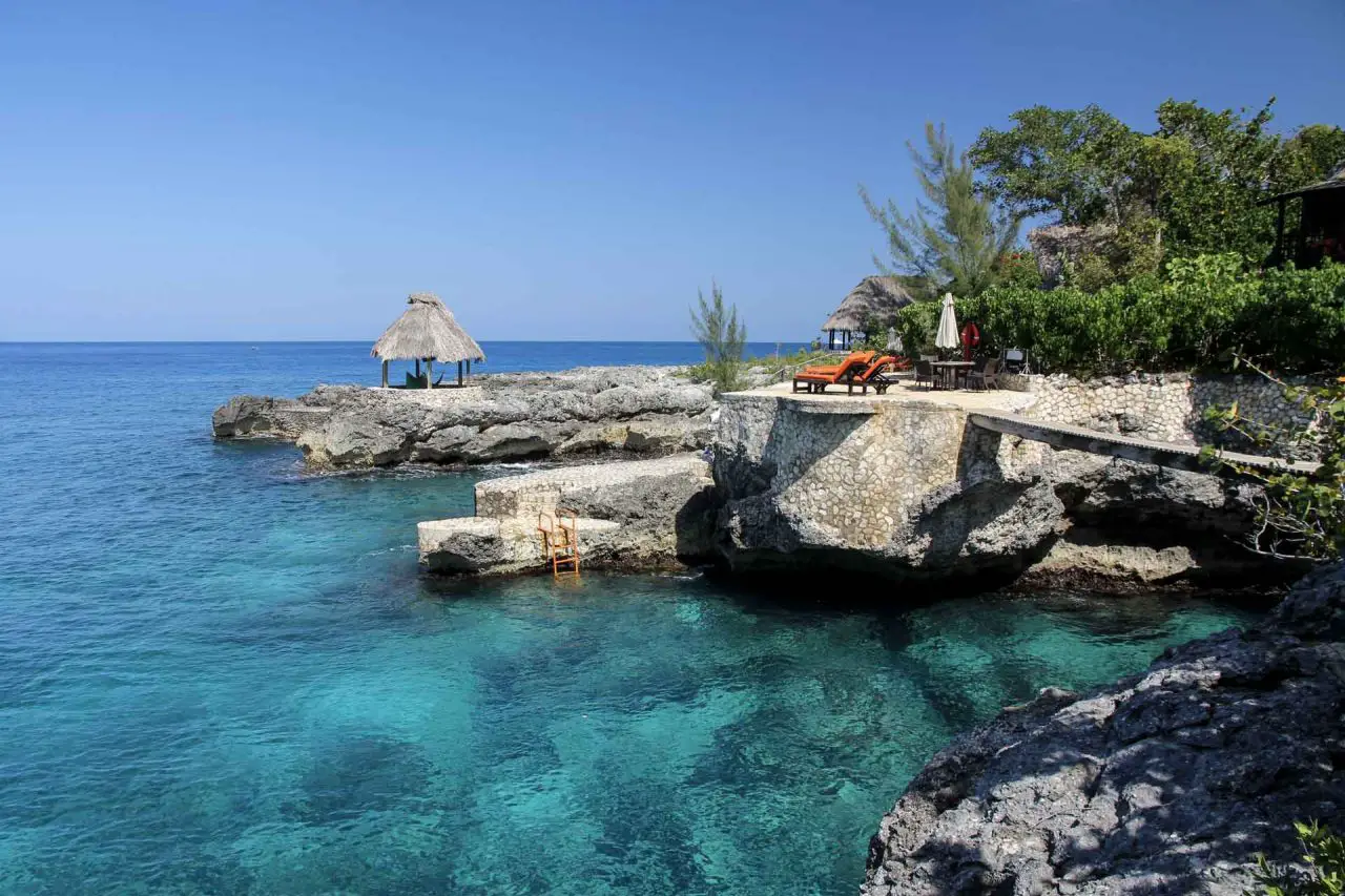 Negril's azure waters and cliffed coastline with orange sun lounges and a tiki hut