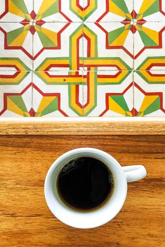 Coffee cup on wooden table with red yellow and green patterned floor tiles below