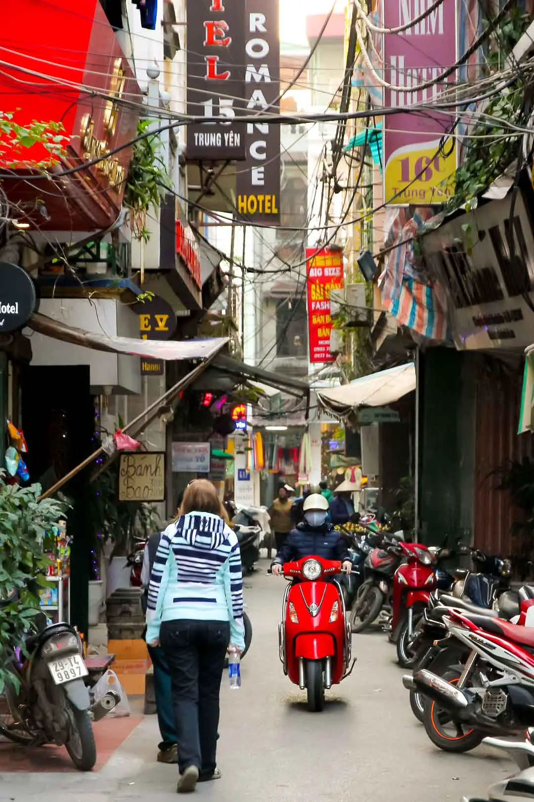 Narrow laneway with restaurant awnings, pedestrians and moped rider