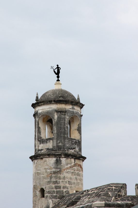 Weather vane in shape of woman holding cross on top of stone tower