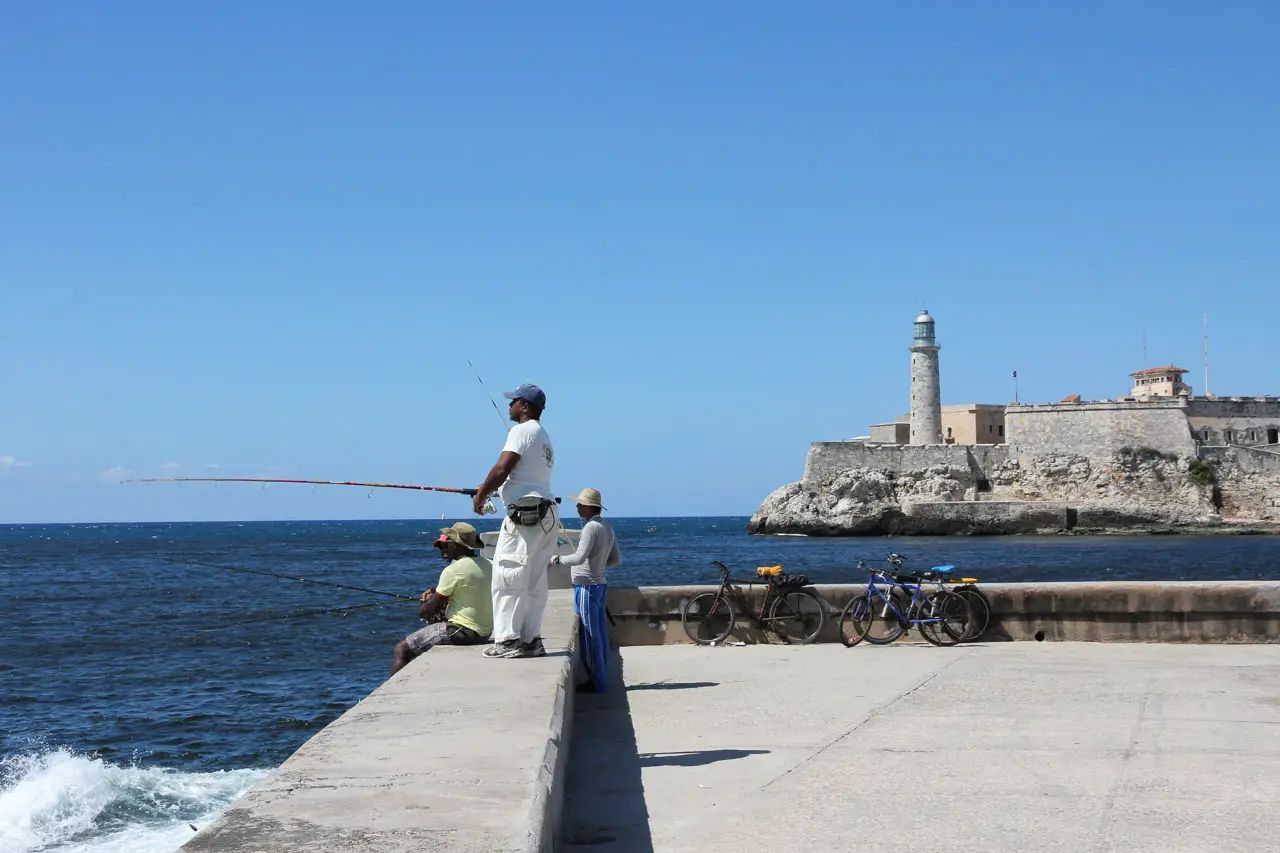 Men fishing on the Malecón with the lighthouse across the channel in the background