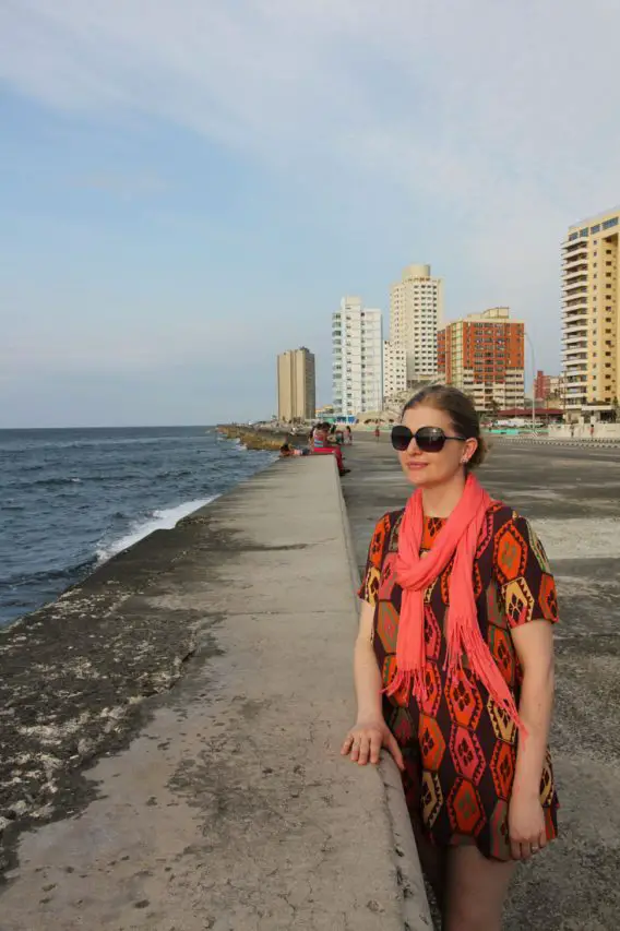Woman in orange toned dress standing at sea wall with highrise buildings in the background
