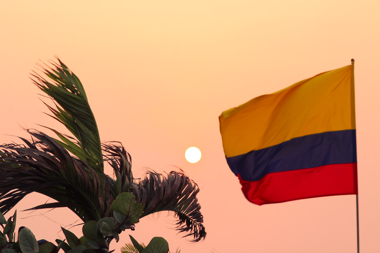 Hazy sunset framed by Colombian flag and a palm tree