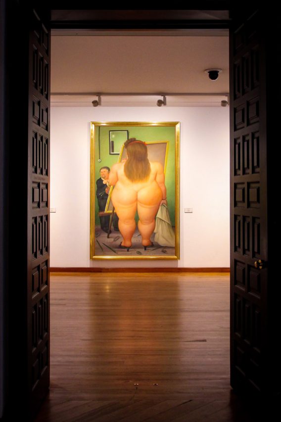 Painting of naked woman from behind viewed through gallery doorway