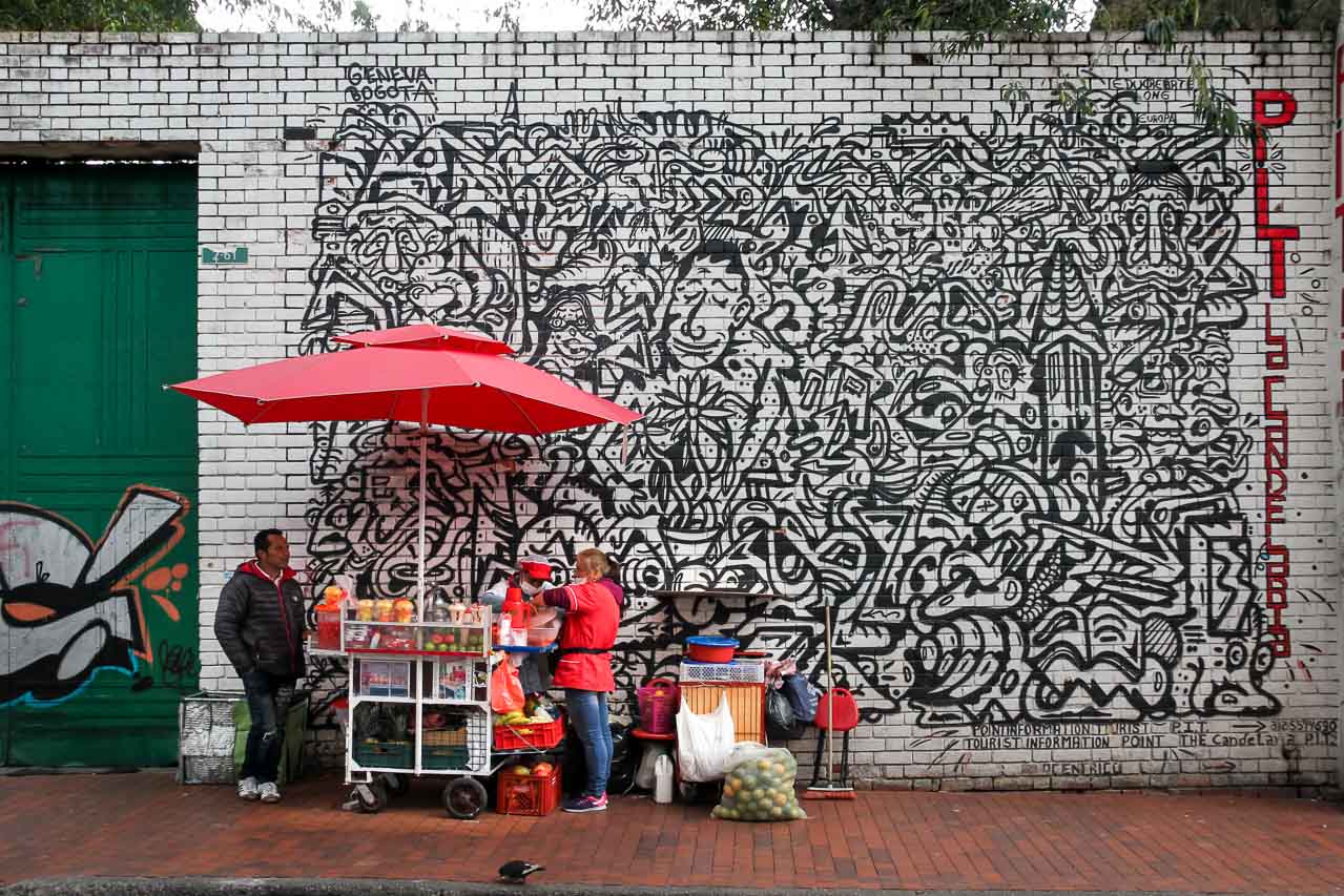 Bogota street vendor with a large red umbrella, set up infront of a labyrinth-like mural