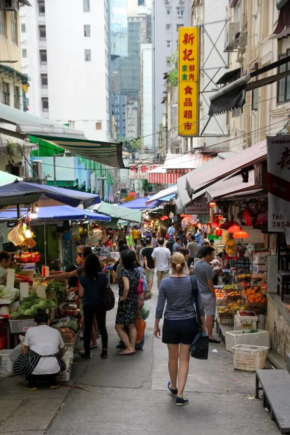 Woman walking towards market selling fruit and vegetables in Hong Kong street