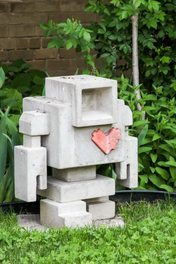 Concrete sculpture of a robot with a red heart on its chest, standing in a garden