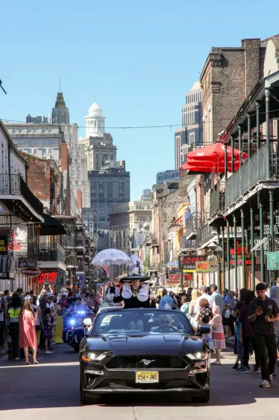 Black car driving up busy Bourbon St with lady in Easter Bonnet and holding a parasol
