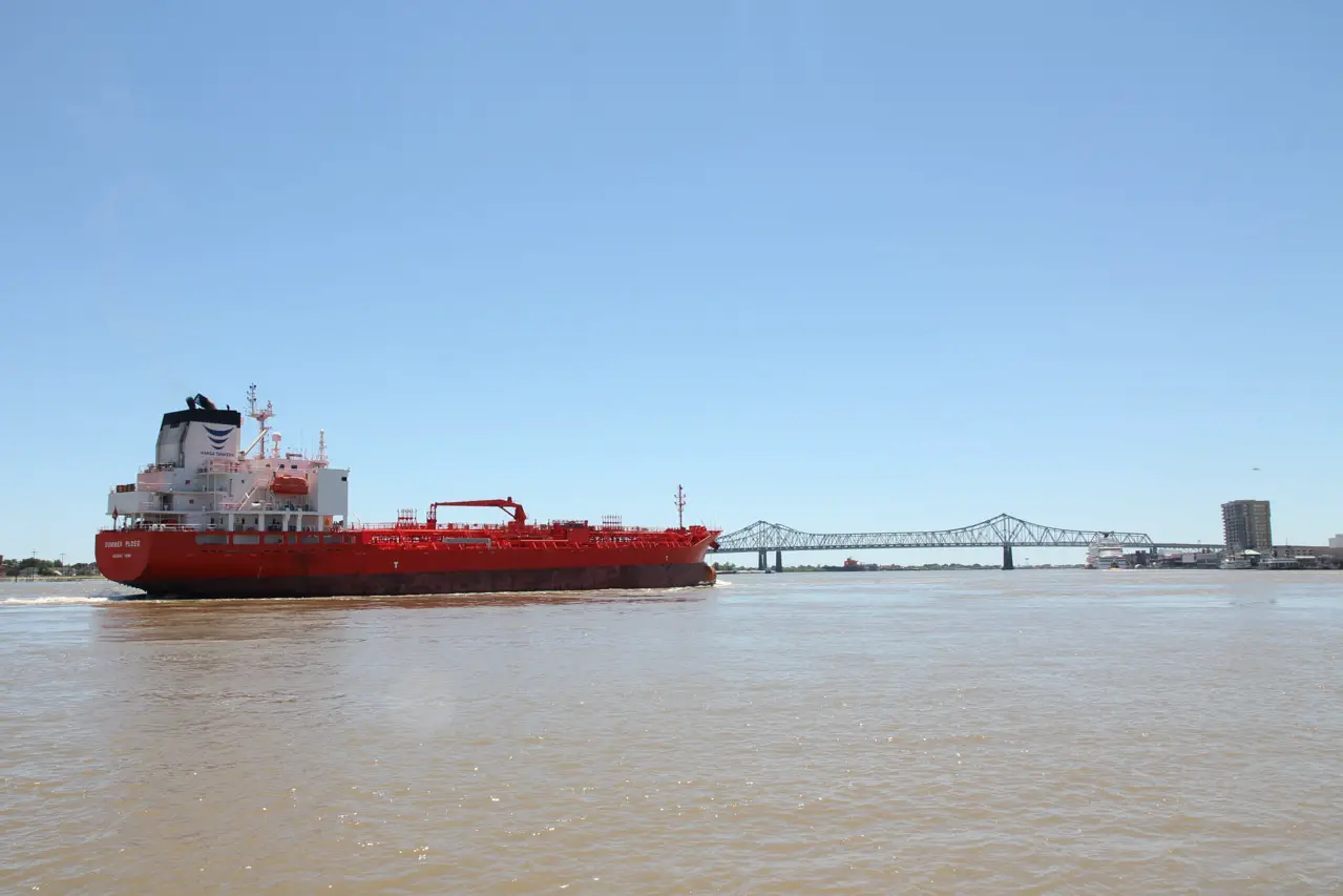 An empty, red cargo ship approaches a large bridge across the Mississippi River