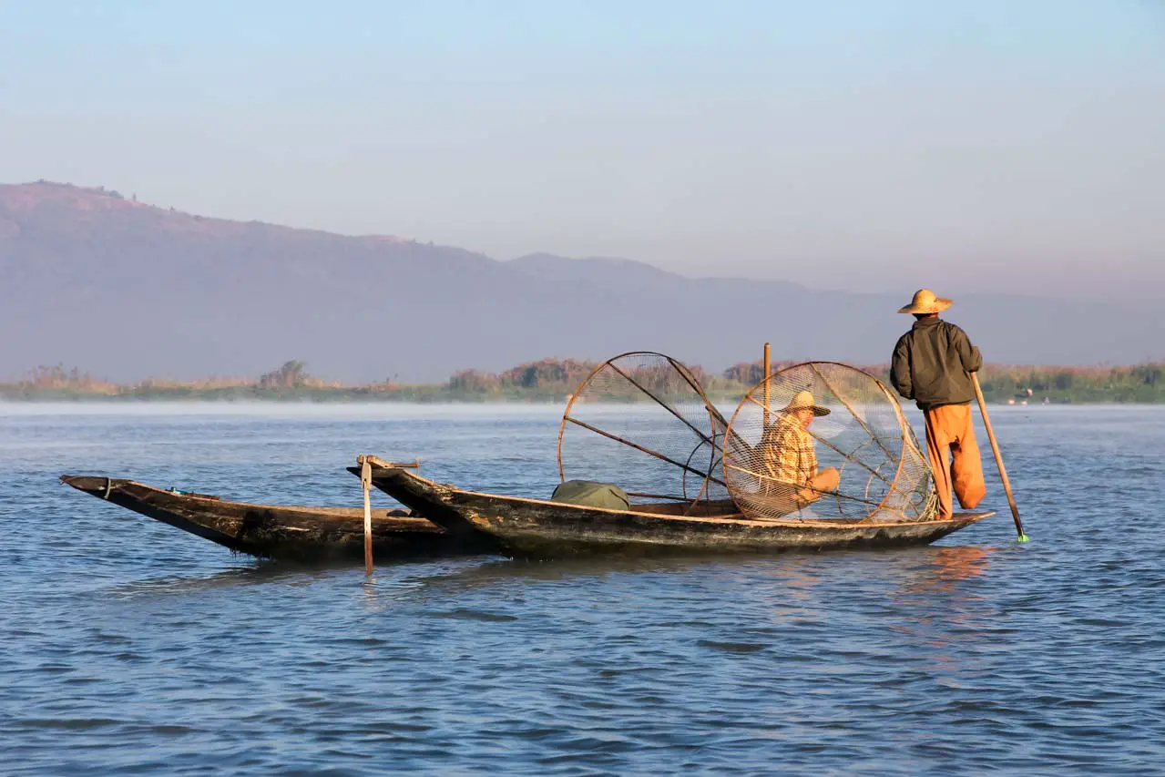 Two fishermen on their boats on a lake with mountains in the background