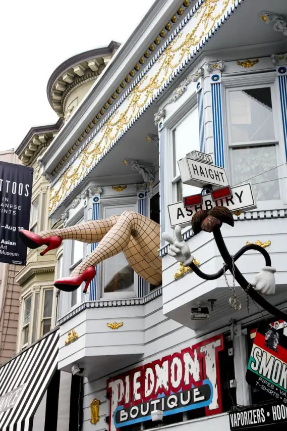 Large ladies legs in fishnets and red stilletos hanging out of second story window over Piedmont Boutique