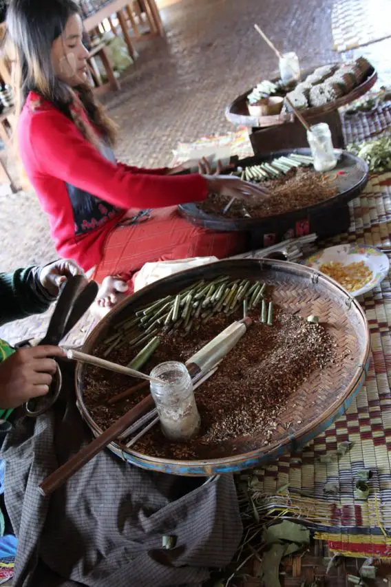 Women hand rolling cigars with large, flat baskets of ingredients