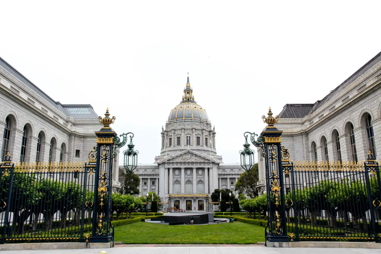 Domed City Hall building viewed between the War Memorial Opera House and Veterans Building with ornate, gold and black gates in foreground