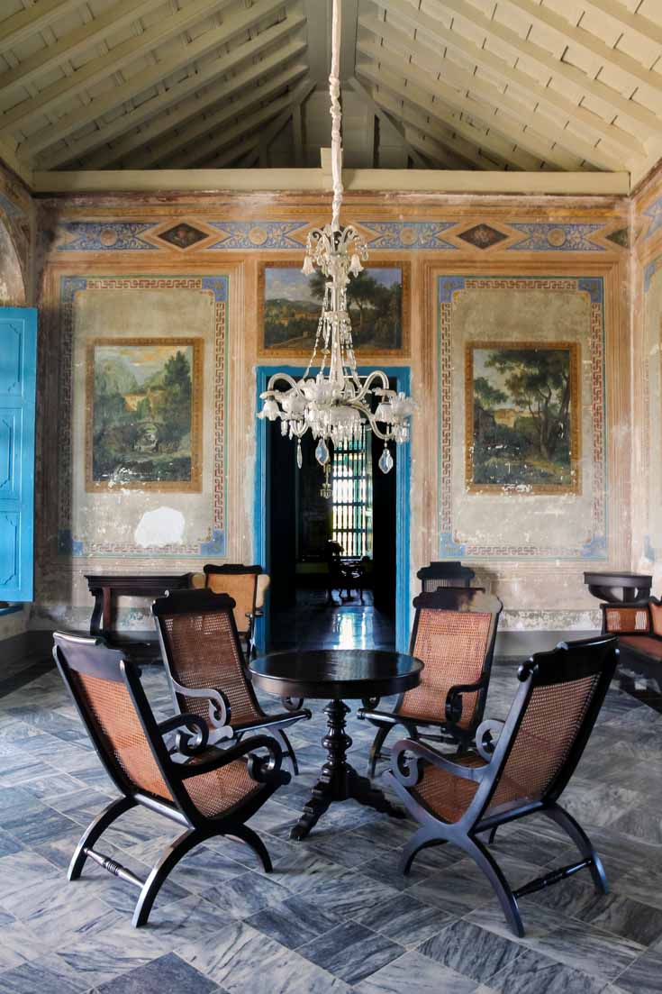 Interior of great house with antique chairs, blue doors, chandelier and faded frescoes